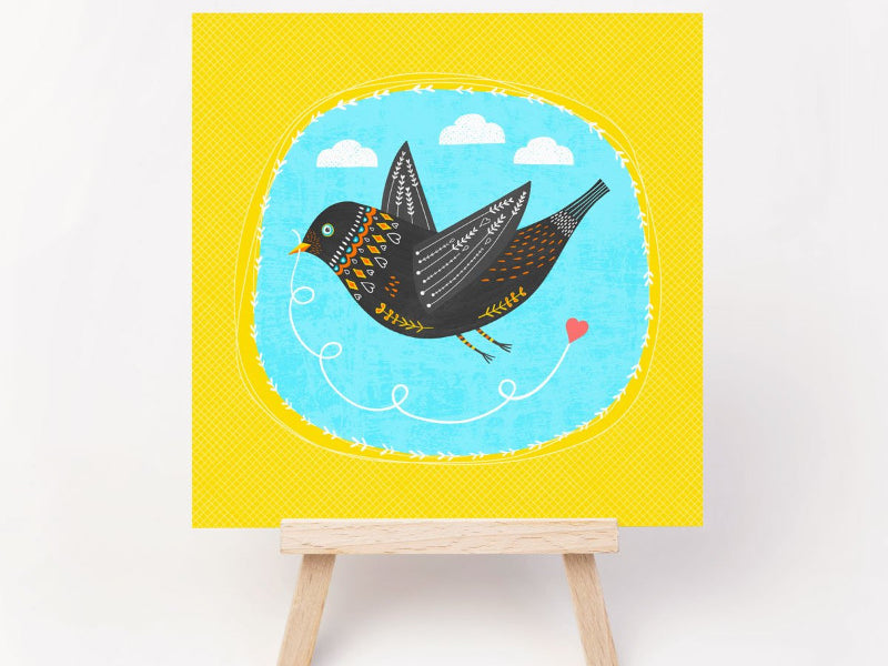 A greeting card of a bright and cheerful card with a love bird pulling along a love heart. Irish made greeting cards by Fleur & Mimi.