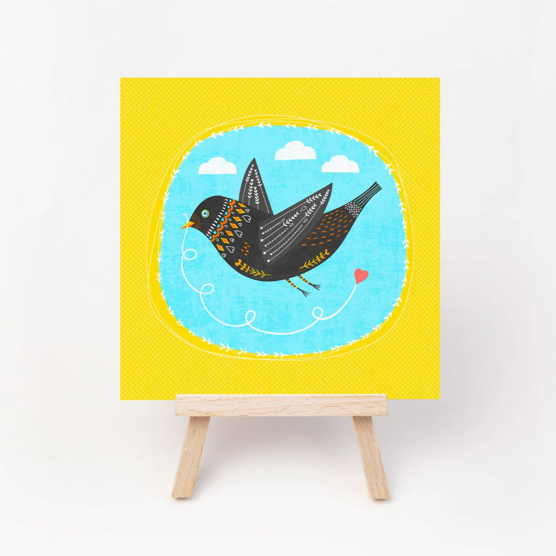 A greeting card of a bright and cheerful card with a love bird pulling along a love heart. Irish made greeting cards by Fleur & Mimi.